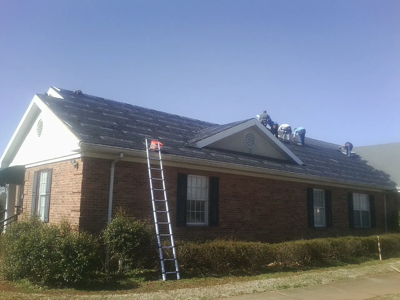 Crew tearing shingles off a brick ranch roof with a ladder set — Metal Roof Repair work by our crew in Piedmont