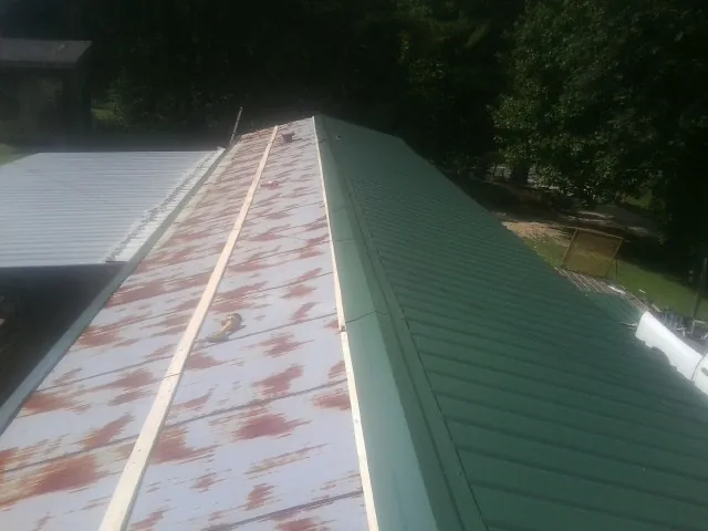 Old rusted panels beside newly installed green metal roofing in Piedmont